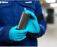 A person wearing gloves and handling a metal cylinder